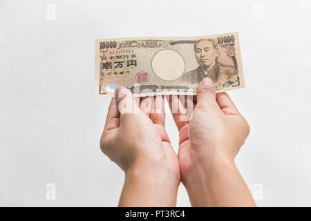 Imprenditrice dando denaro e tenendo 10.000 yen giapponese soldi in mano isolati su sfondo bianco, yen giapponese finanziaria e la concezione di business Foto Stock