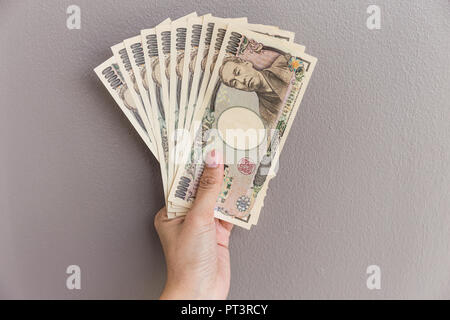 Imprenditrice dando denaro e tenendo 10.000 yen giapponese soldi in mano sul muro grigio Sfondo, yen giapponese finanziaria e la concezione di business Foto Stock