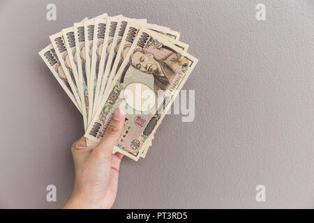 Imprenditrice dando denaro e tenendo 10.000 yen giapponese soldi in mano sul muro grigio Sfondo, yen giapponese finanziaria e la concezione di business Foto Stock