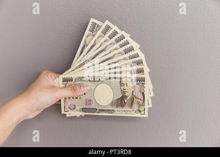 Imprenditrice dando denaro e tenendo 10.000 yen giapponese soldi in mano sul muro grigio Sfondo, yen giapponese finanziaria e la concezione di business Foto Stock