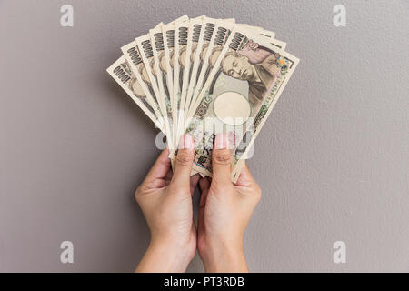 Imprenditrice dando denaro e tenendo 10.000 yen giapponese soldi in mano sul muro grigio Sfondo, yen giapponese finanziaria e la concezione di business Foto Stock