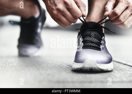 Immagine ritagliata di mani lacci delle scarpe di legatura su sneaker, superficie in esecuzione sullo sfondo. Le mani di uno sportivo con contapassi lacci delle scarpe di legatura su sneaker sportiva. Ru Foto Stock