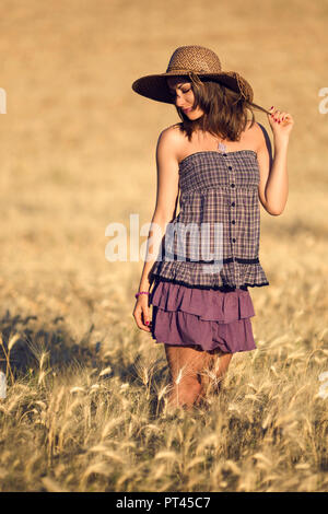 Brunette donna in abito viola in un campo di grano al tramonto, marche, Italia Foto Stock