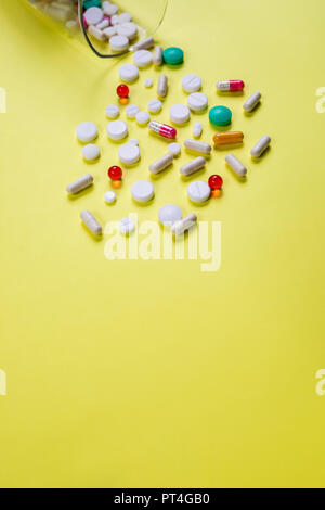 Concetto di malattia. No alla droga e pillole concetto. Il confezionamento di compresse e pillole sul tavolo. Pila di capsule sparse su sfondo giallo.colorata capsule isolato, farmacia pillola flacone di farmaco concetto.spazio copia Foto Stock