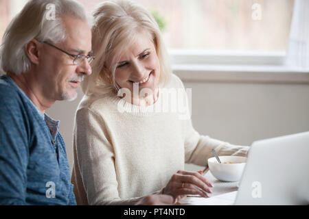 Senior coppia felice godendo utilizzando laptop mangiare insieme per la prima colazione, sorridente centro anziani di età compresa tra famiglia shopping online, la lettura di discutere di internet n Foto Stock