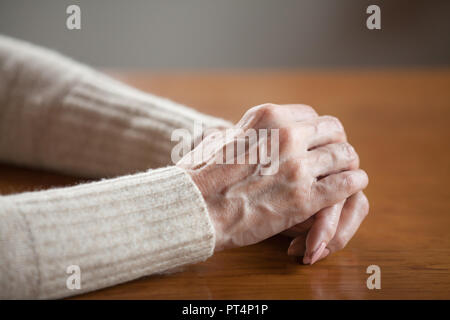 Vista ravvicinata di matura vecchia persona femmina stropicciata mani con vene sul tavolo, sono di mezza età senior donna anziana tenendo le braccia incrociate pregando come concetto Foto Stock