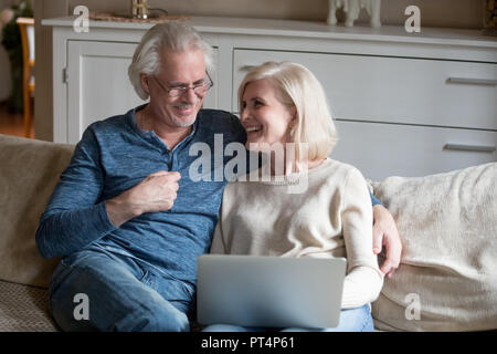 Senior felice coppia di mezza età ridere rilassante con computer portatile in salotto, anziani vecchia famiglia maturi godersi divertenti umorismo online sorridente divertendosi Foto Stock