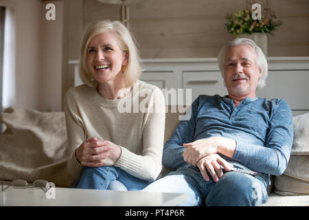 Senior felice coppia di mezza età ridere guardando umorismo programma tv tenendo premuto Controllo remoto seduto sul divano nel soggiorno, sorridente coppia familiare godetevi Foto Stock