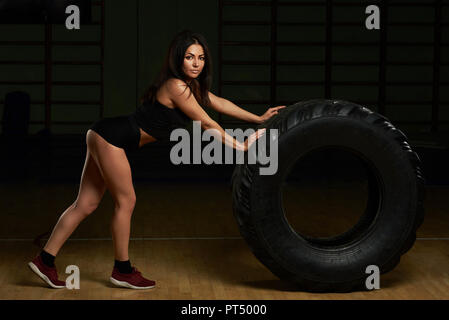 Bella bruna con pneumatico in palestra sfondo. Giovane donna fare fitness Foto Stock