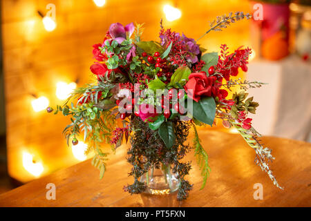 Composizione floreale con bacche rosse, rose rosse e verdi sul tavolo Foto Stock