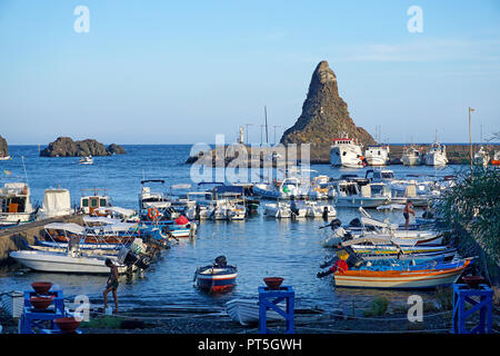 Barche da pesca al porto di Aci Trezza, dietro la roccia di basalto Faraglione grande, Isole dei Ciclopi, comune di Aci Castello, Catania, Sicilia, Ita Foto Stock