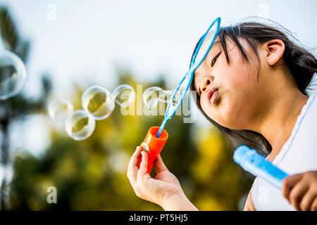 Ragazza a soffiare bolle con bolla di bacchetta magica nel parco. Foto Stock