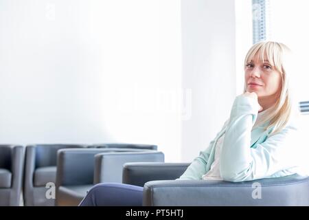 Malinconici metà donna adulta in seduta del medico sala di attesa con la mano sul mento. Foto Stock