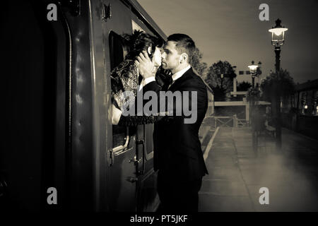 Vintage giovane, uomo bello in uniforme, kissing addio il suo amante sulla stazione ferroviaria piattaforma come il treno sta per partire. Foto Stock