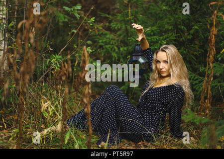 La bionda nella foresta. Nelle mani di una ragazza con una lanterna vintage Foto Stock