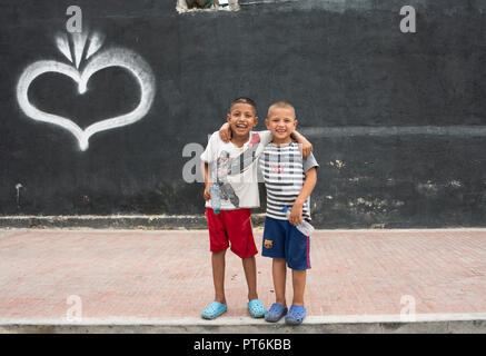 Due allegri ragazzi amichevoli si abbracciano con un grande sorriso e bottiglie di plastica vuote nelle loro mani. Santa Marta, Colombia. Set 2018 Foto Stock