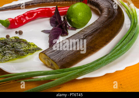 Still Life - aguglia affumicato con calce, basilico, cipollotti, peperoncino, nori chips, spezie, olio d'oliva in un bianco piatto di ceramica, su di un tavolo di legno Foto Stock