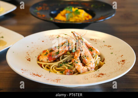 Cibo sano concetto. Spaghetti con gamberetti, gamberi e basilico tritato e pomodoro su piastra bianca. Piastre di sfocatura con alimenti sfondo. Foto Stock