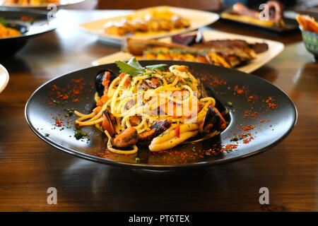 Cibo sano concetto. Spaghetti con gamberi, gamberetti, cozze e prezzemolo sulla piastra nera. Piastre di sfocatura con alimenti sfondo. Foto Stock