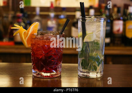 Concetto di bevande. Trasparente a freddo cocktail con cubetti di ghiaccio con il nero cannucce. Bottiglie di sfocatura sullo sfondo, vista ravvicinata. Foto Stock