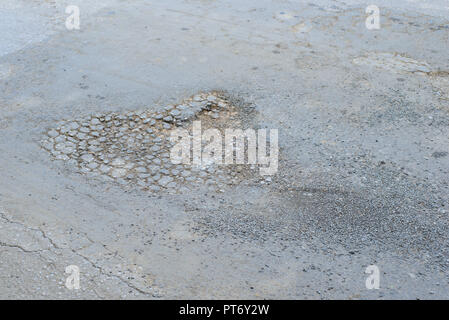 Fossa di grandi dimensioni con pietre sulla strada asfaltata Foto Stock