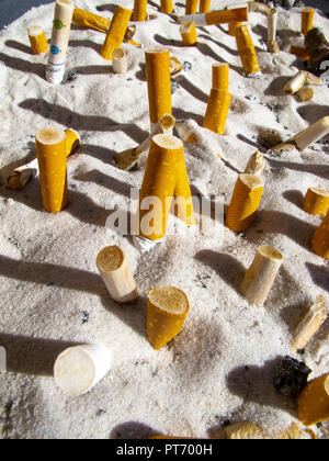 Mozziconi di sigarette spente in un posacenere con sabbia bianca Foto Stock