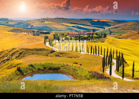 Incredibile tramonto colorato in Toscana. Il pittoresco agriturismo e tipica strada curva con i cipressi, Crete Senesi Paesaggio rurale in Toscana, Italia, Euro Foto Stock