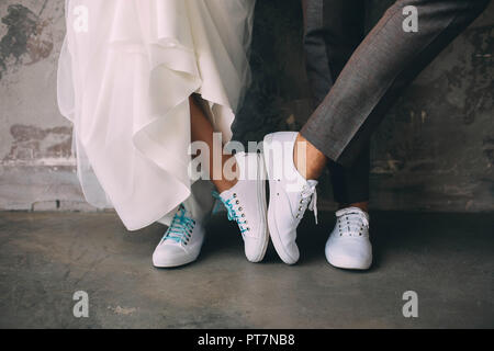 Ritagliato maschio e femmina gambe indossando sneakers bianco. Nozze in sneakers Foto Stock