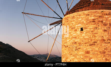 Un vecchio mulino in pietra sulla cima di una montagna, contro lo sfondo di una catena montuosa e a valle con un piccolo borgo di case bianche su un isola greca Foto Stock