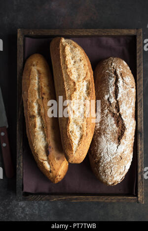 Varie freschi fatti in casa pane rustico in cassetta di legno, vista dall'alto, copia dello spazio. Pasta madre mini baguette di frumento e pane di segale. Foto Stock