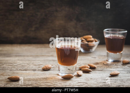 Liquore italiano Amaretto con mandorle in legno rustico sfondo, spazio di copia Foto Stock