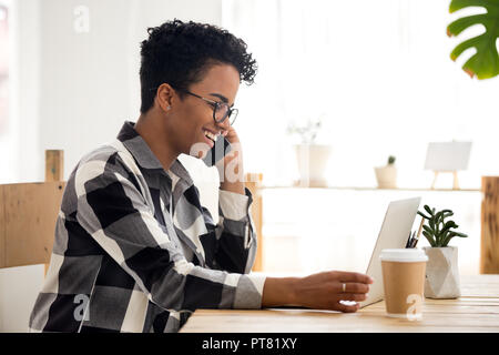 Donna sorridente a lavorare utilizzando il computer e il telefono in ufficio Foto Stock
