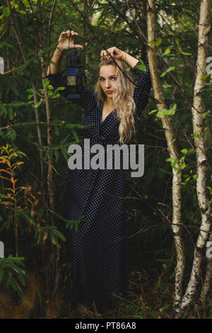 La bionda nella foresta. Nelle mani di una ragazza con una lanterna vintage Foto Stock