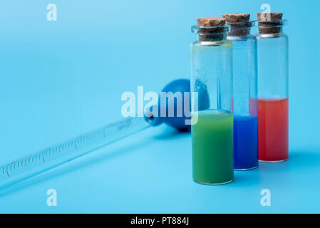 Provette con liquido diverso all'interno su sfondo blu. Il liquido nel tubo di prova è di colore rosso, verde e blu. Foto Stock