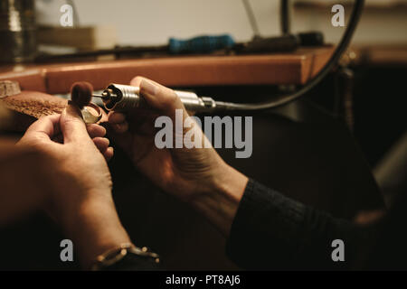 Femmina matura gioielliere la lucidatura di un anello d'oro al banco di lavoro. Goldsmith facendo un anello al suo lavoro negozio utilizzando strumenti. Stretta di mano del Creatore di gioielli usi Foto Stock