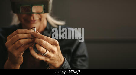 Femmina ispezionando orafo gioielli con lente di ingrandimento in officina. Donna gioielliere ispezione corona diamantata con lente di ingrandimento. Foto Stock