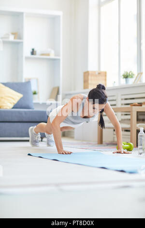 Montare brunette girl facendo push-up sul tappetino durante l esercizio nel salotto di casa Foto Stock