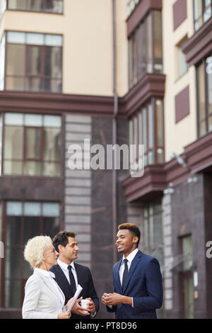 Fiducioso bello imprenditore africani in tuta la condivisione del suo piano creativo con i colleghi mentre si sta in piedi in edificio per uffici, multietnico business Foto Stock