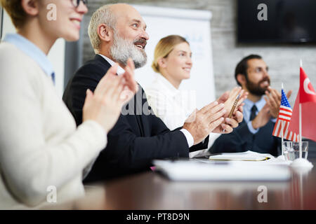 Fila di imprenditori di successo battendo le mani dopo relazione o parlato di uno dei delegati a una conferenza Foto Stock