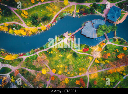 Vista aerea di incredibile autunno parco con laghetto in Europa al tramonto. Paesaggio con alberi con foglie colorate, edifici, campo con erba verde e pat Foto Stock
