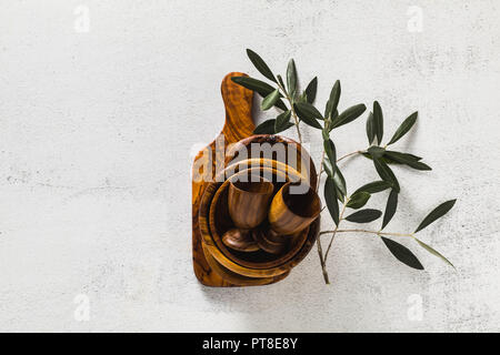 Utensili di legno di ulivo sul bianco tavolo da cucina e i rami di ulivo. eco-friendly kitchenware Foto Stock