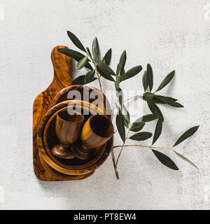 Utensili di legno di ulivo sul bianco tavolo da cucina e i rami di ulivo. eco-friendly kitchenware Foto Stock