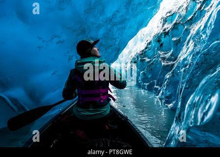 Una donna nella parte anteriore di una canoa soste per apprezzare il limpido blu ghiaccio nelle pareti di una caverna di ghiaccio. Valdez glacier ice cave nel 2016 Foto Stock