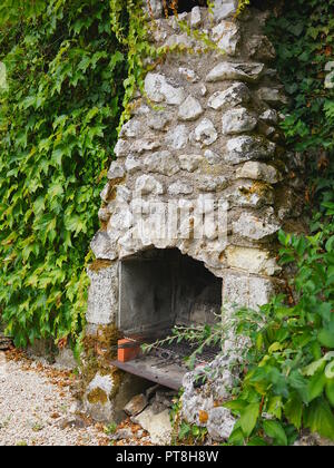 Barbeqcue nel camino di pietra immerso nel verde e frondosa parete in cortile Foto Stock