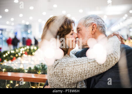 Una felice coppia senior in piedi nel centro commerciale, baciare. Foto Stock