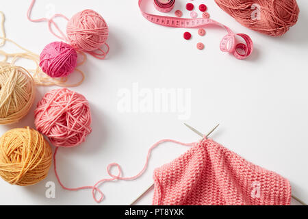 Progetto di lavorazione a maglia in corso. Un pezzo di maglia con sfera di filato e di aghi di tessitura. Foto Stock