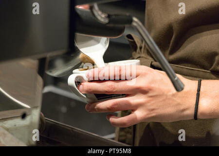 Close-up di femmina mani barista versando il latte caldo in una tazza per fare un cappuccino. Foto Stock