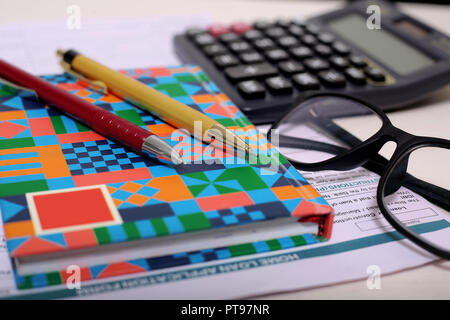Immagine della calcolatrice, due penne, notebook, forma e bicchieri. Foto Stock
