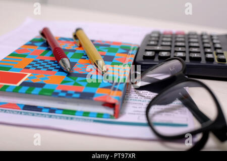 Immagine del modulo, notebook, due penne, calcolatrice e bicchieri. Foto Stock