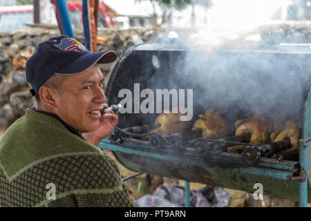 Mercato all'aperto a San Bartolome village nr Cuenca Ecuador - uomo tostatura di pollo allo spiedo Foto Stock